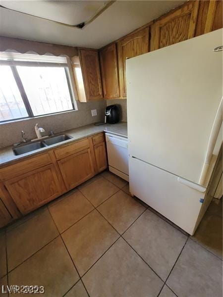 kitchen featuring light tile patterned floors, white appliances, a sink, light countertops, and brown cabinets