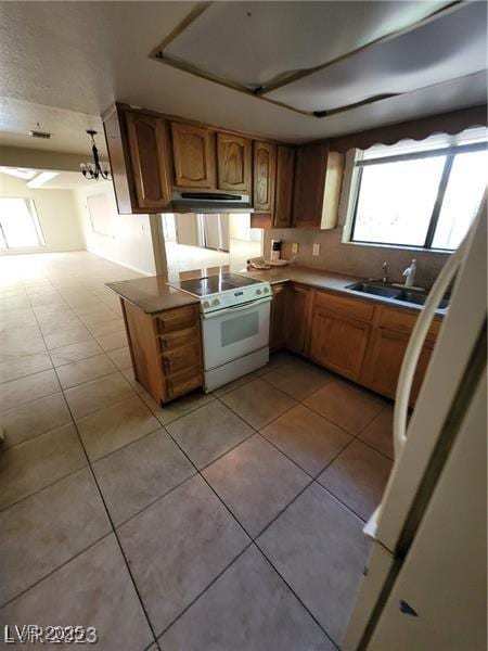 kitchen featuring light tile patterned flooring, under cabinet range hood, white appliances, a sink, and brown cabinetry