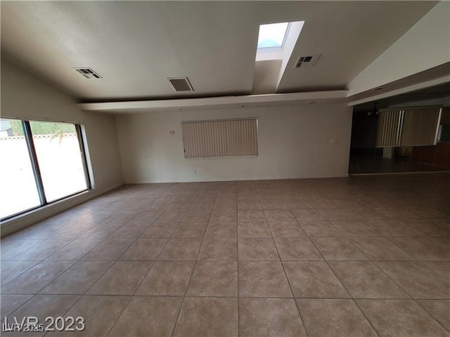 tiled spare room with lofted ceiling with skylight and visible vents