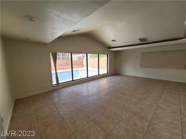 spare room with vaulted ceiling, visible vents, and tile patterned floors