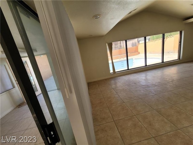 tiled spare room featuring lofted ceiling and baseboards