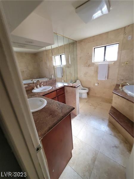 full bath with double vanity, toilet, a bathing tub, a sink, and tile walls