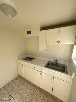 kitchen with light countertops, light tile patterned flooring, a sink, and white cabinetry