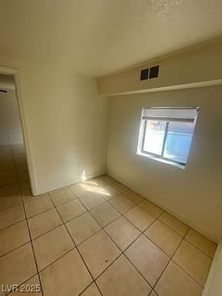 empty room with visible vents, a textured ceiling, and light tile patterned floors