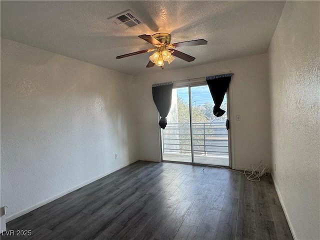 unfurnished room featuring a textured ceiling, visible vents, dark wood-style flooring, and a textured wall