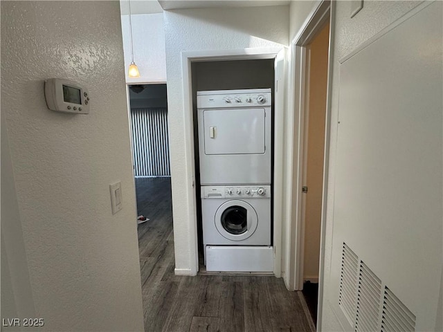 laundry room with laundry area, stacked washer and clothes dryer, a textured wall, and wood finished floors