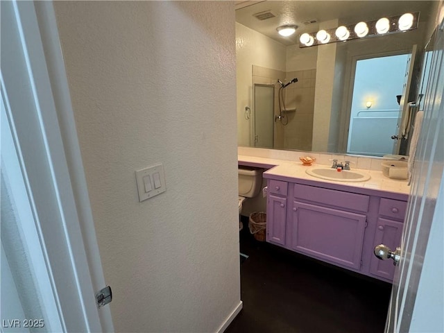 full bath with visible vents, a textured wall, walk in shower, and vanity