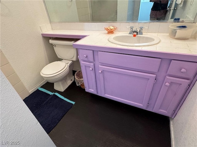 bathroom featuring a textured wall, vanity, and toilet