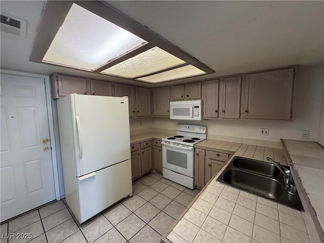 kitchen featuring tile countertops, visible vents, light tile patterned flooring, a sink, and white appliances