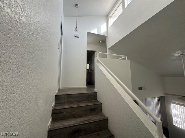 stairs with a towering ceiling, visible vents, and a textured wall