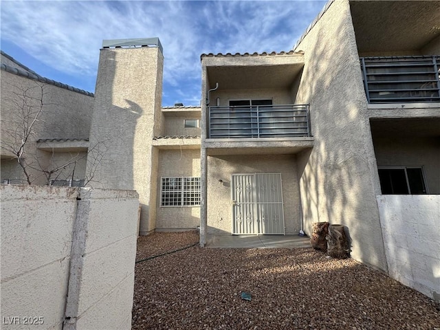 back of house with a balcony, a patio, and stucco siding