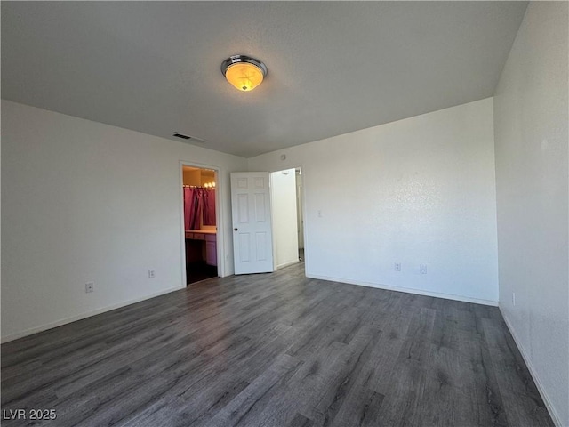 unfurnished bedroom with baseboards, visible vents, dark wood-style flooring, and ensuite bathroom