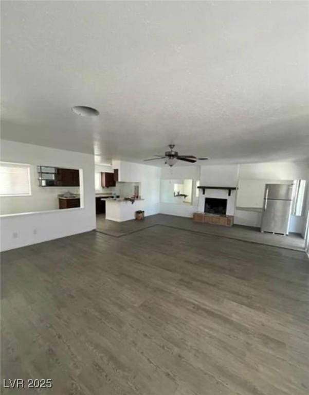 unfurnished living room featuring a fireplace with raised hearth, ceiling fan, a textured ceiling, and wood finished floors