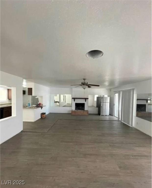 unfurnished living room with a fireplace with raised hearth, ceiling fan, and wood finished floors