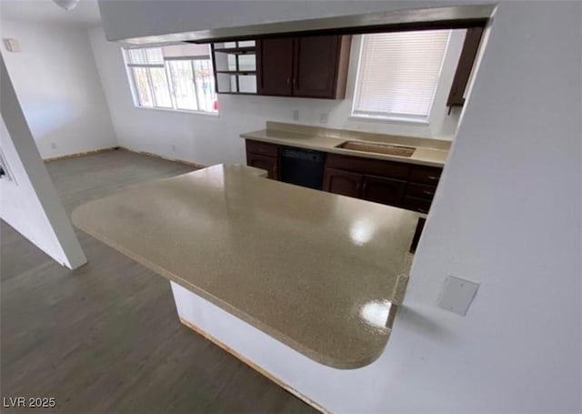 kitchen with dark brown cabinetry, a peninsula, wood finished floors, a sink, and black dishwasher