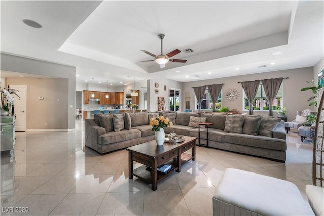 living area featuring a tray ceiling, recessed lighting, visible vents, and baseboards