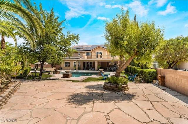 back of property featuring an outdoor pool, a patio area, fence, and roof mounted solar panels