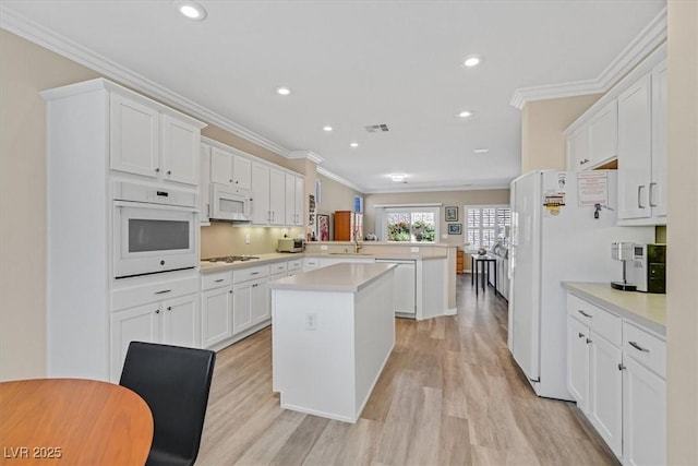 kitchen with a peninsula, white appliances, a kitchen island, visible vents, and light countertops