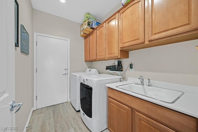 clothes washing area featuring a sink, light wood-type flooring, washing machine and clothes dryer, and cabinet space