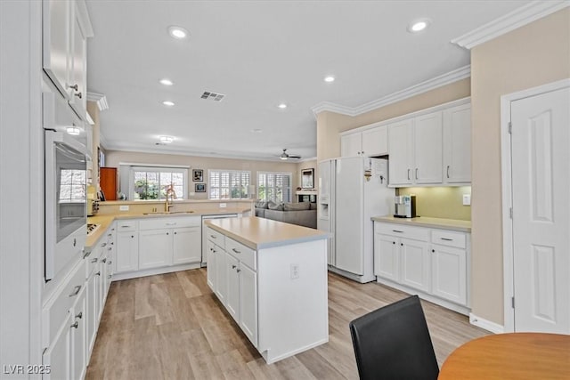 kitchen featuring visible vents, light countertops, crown molding, white fridge with ice dispenser, and a sink