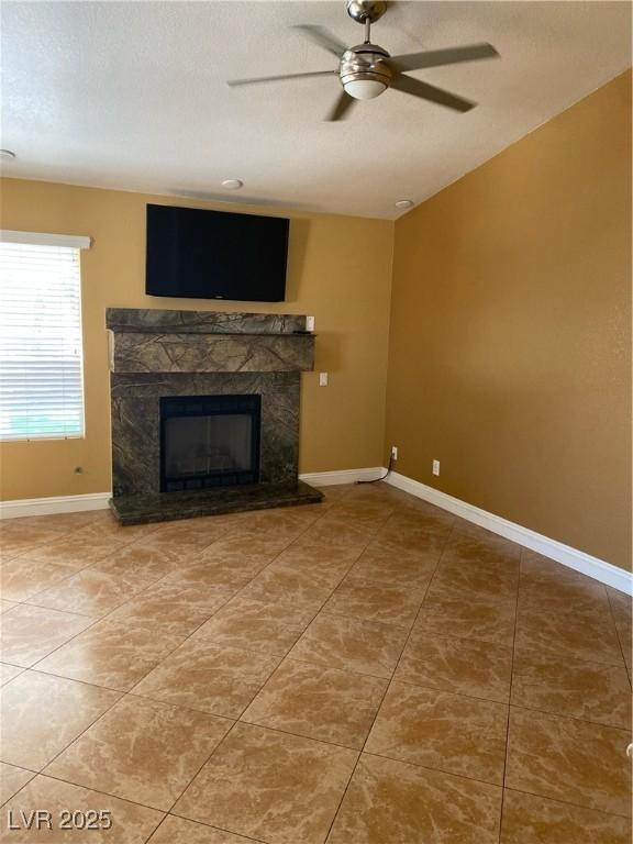 unfurnished living room featuring a textured ceiling, tile patterned flooring, a high end fireplace, baseboards, and a ceiling fan