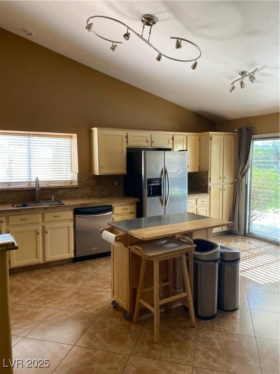 kitchen featuring lofted ceiling, a kitchen island, appliances with stainless steel finishes, a sink, and backsplash