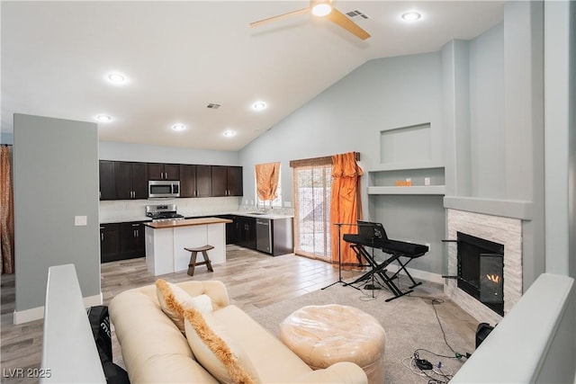 living room with a fireplace, visible vents, light wood-style floors, a ceiling fan, and high vaulted ceiling