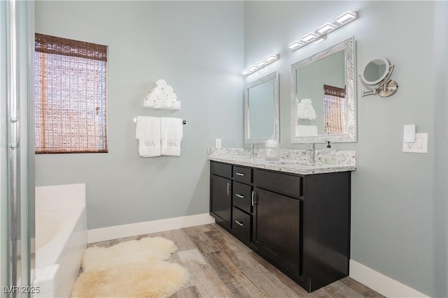 full bathroom featuring double vanity, a sink, wood finished floors, baseboards, and a bath