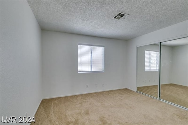 unfurnished bedroom featuring a closet, visible vents, a textured ceiling, and carpet flooring