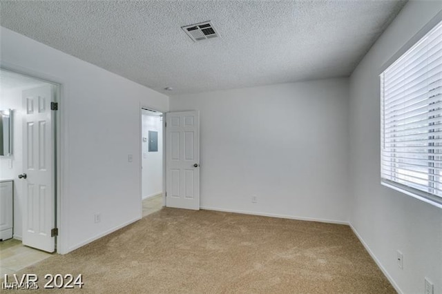 unfurnished room with light carpet, a textured ceiling, visible vents, and baseboards