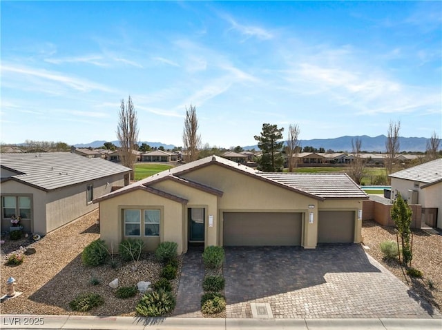 single story home with decorative driveway, stucco siding, an attached garage, a mountain view, and a tiled roof