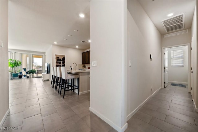 corridor featuring recessed lighting, baseboards, visible vents, a sink, and light tile patterned flooring