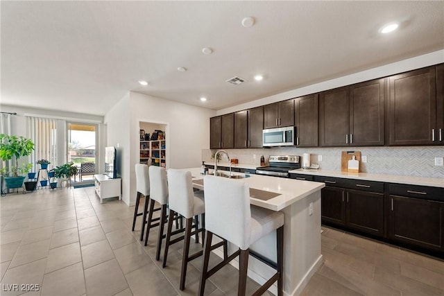 kitchen featuring stainless steel appliances, tasteful backsplash, visible vents, a sink, and a kitchen bar