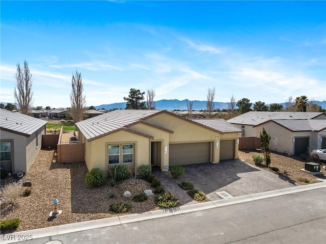 ranch-style house featuring a garage, fence, decorative driveway, a mountain view, and stucco siding