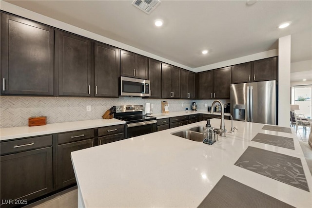 kitchen with visible vents, decorative backsplash, appliances with stainless steel finishes, dark brown cabinets, and a sink