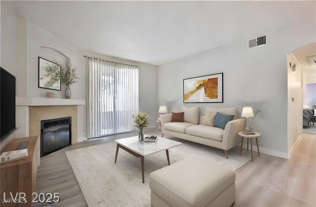 living room with visible vents, arched walkways, light wood-style floors, and a glass covered fireplace