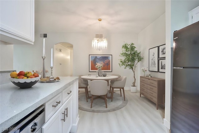 dining space featuring arched walkways, visible vents, light wood-type flooring, and a chandelier