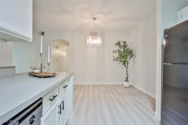 kitchen with visible vents, baseboards, arched walkways, freestanding refrigerator, and white cabinets