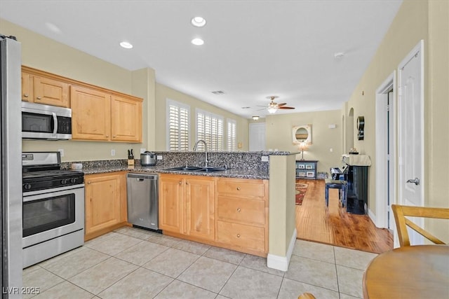 kitchen with light tile patterned floors, appliances with stainless steel finishes, a peninsula, light brown cabinets, and a sink