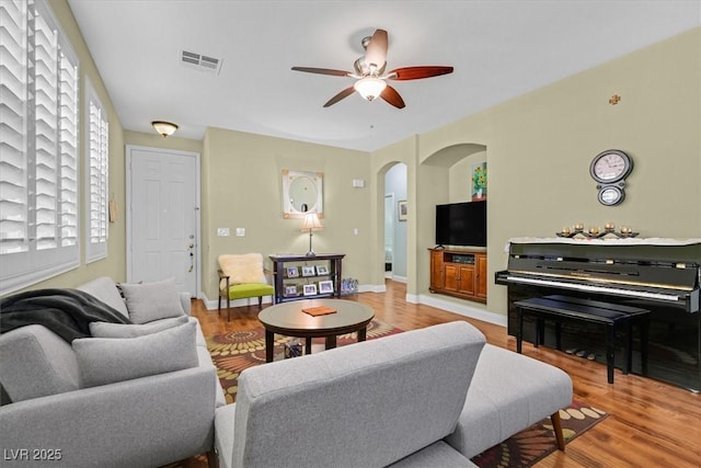 living room with light wood finished floors, baseboards, visible vents, arched walkways, and ceiling fan