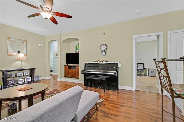 living area featuring a ceiling fan, baseboards, arched walkways, and wood finished floors