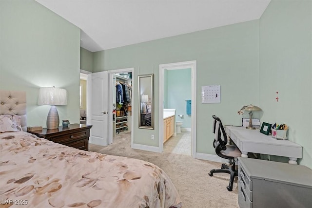 bedroom with a closet, light colored carpet, a spacious closet, ensuite bath, and baseboards