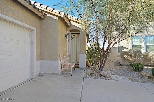 view of exterior entry featuring a garage, a tile roof, a patio, and stucco siding