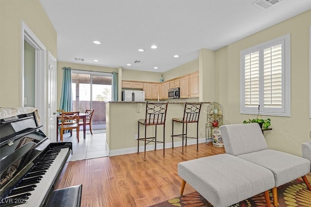 kitchen featuring stainless steel microwave, visible vents, light brown cabinetry, freestanding refrigerator, and a kitchen bar