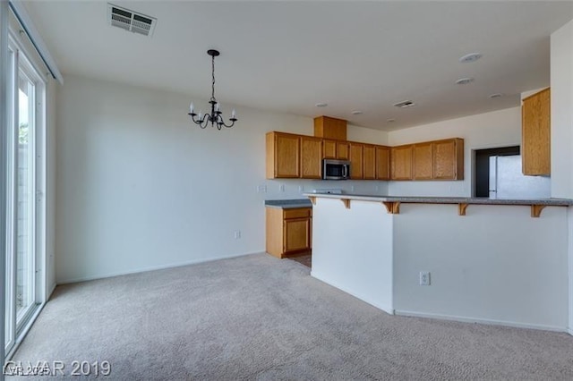 kitchen featuring visible vents, light colored carpet, stainless steel microwave, a breakfast bar area, and freestanding refrigerator