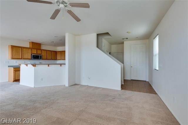 unfurnished living room with light carpet, stairs, visible vents, and a ceiling fan