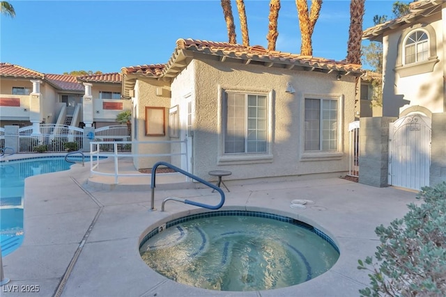 community pool with a patio, fence, a gate, and a hot tub