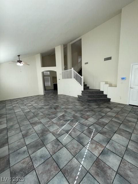 unfurnished living room with arched walkways, ceiling fan, high vaulted ceiling, and stairs