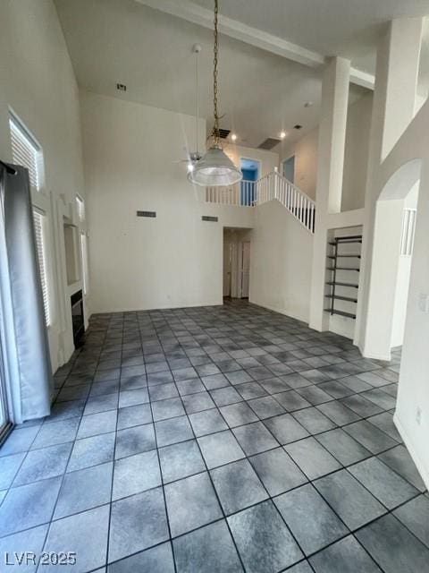 interior space featuring arched walkways, tile patterned flooring, a towering ceiling, stairway, and plenty of natural light