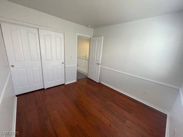 unfurnished bedroom featuring dark wood-type flooring, a closet, and baseboards